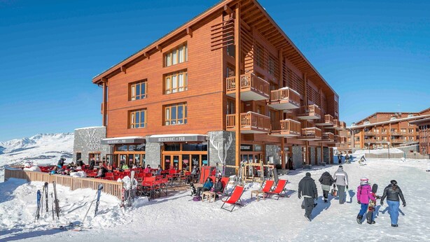 Ein mehrstöckiges Gebäude mit Holzfassade, einer Außenbestuhlung und Skiausrüstung.