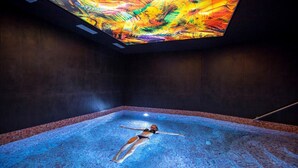 Eine Person treibt in einem großen, überdachten Pool unter einer farbenfrohen Decke.