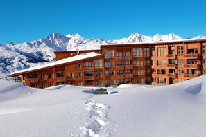 A multi-story wooden hotel with balconies, set against a backdrop of snow-covered mountains.