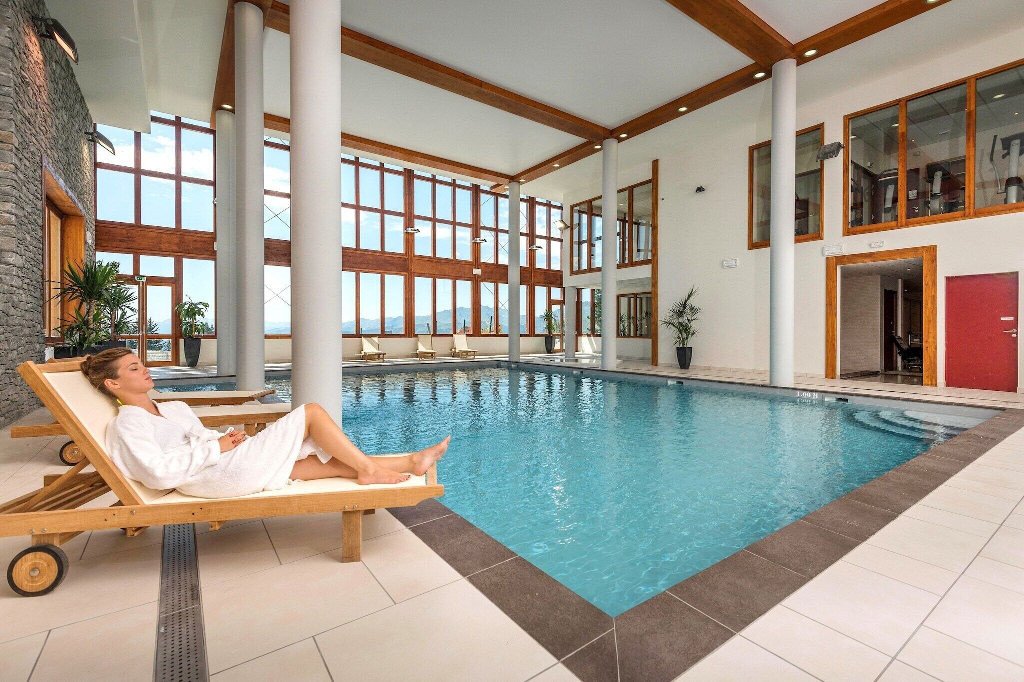 A large indoor swimming pool with a person relaxing on a lounge chair.
