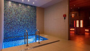 Ein Wellnessbereich mit einer Mosaikwand, einem kleinen Pool und einem Zugang zur Sauna.