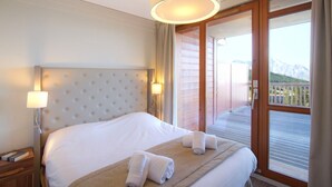 Ein Hotelzimmer mit einem großen Bett, einem Nachttisch, einer Lampe und Blick auf einen Balkon mit Bergen.
