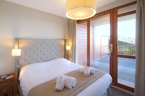 A hotel room with a large bed, a nightstand, a lamp, and a view of a balcony with mountains. - Cozy Suite on the Slopes (Bourg-Saint-Maurice)