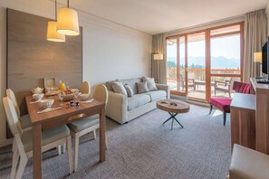 A hotel room with a dining area, a sofa, a small table, and a balcony with a view.