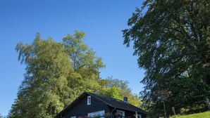 A rustic cabin with a sloped roof, surrounded by lush greenery and trees. - Cozy Chalet in Francorchamps (Stavelot-Neuville)