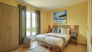 Een slaapkamer met een bed, nachtkastje, lamp, schilderij en raam met gordijnen.