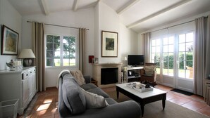 A living room with a sofa, coffee table, fireplace, television, and large windows. - Villa with garden near beautiful golf course (Vasles)