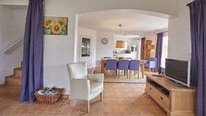 Ein Wohnzimmer mit Fernseher, einem Essbereich und einer Küche im Hintergrund.