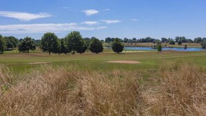 Ein Golfplatz mit Teich, Bäumen und blauem Himmel.
