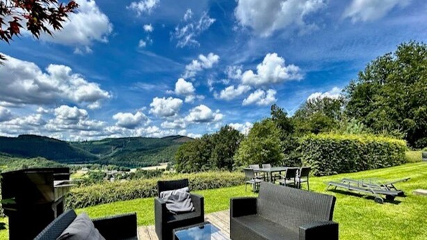 An outdoor seating area with wicker furniture, a table, and a view of a lush landscape with hills and trees. - Villa in Coo with Pool & Panoramic Views (Coo - Stavelot)