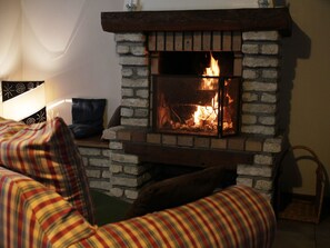 A fireplace with a fire, a couch, and a chair in a room.