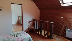 A room with a sloped ceiling, wooden walls, a small table with a floral tablecloth, a chair, and a radiator. - Holiday Home in Quend near Forest and Sea (Quend-Plage)