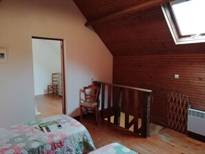 Ein Zimmer mit schrägen Wänden, Holzwänden, einem kleinen Tisch mit Blumenmuster und einem Stuhl, sowie einem Heizkörper.