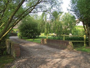 A gravel path leading through a park with a wooden bridge and a brick wall on one side. - Holiday Home in Quend near Forest and Sea (Quend-Plage)