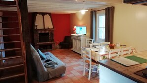 A cozy living room with a fireplace, a dining area with a table and chairs, and a TV on a stand. - Holiday Home in Quend near Forest and Sea (Quend-Plage)