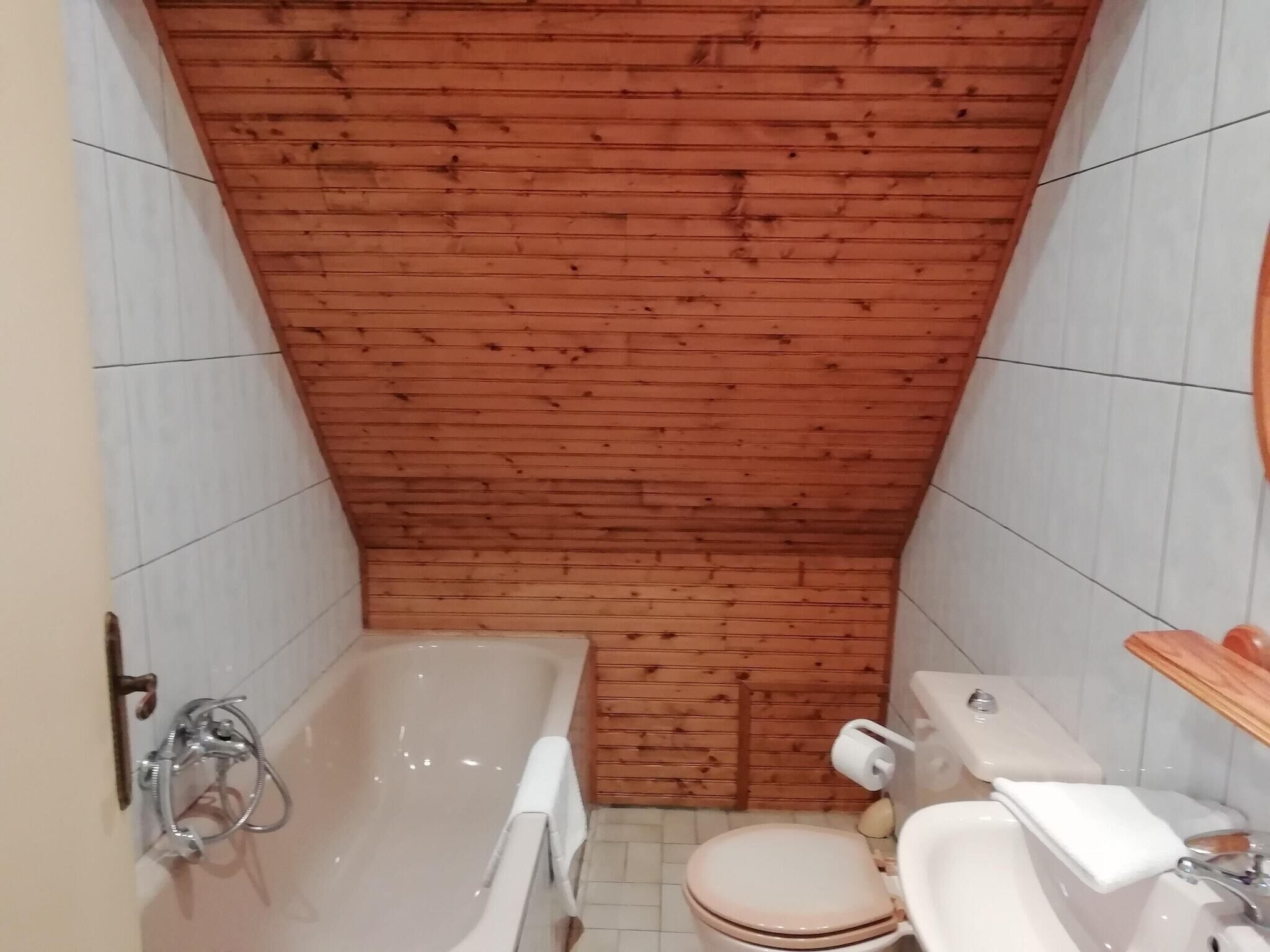 Une petite salle de bain avec un plafond en bois, une baignoire, des toilettes et un lavabo.