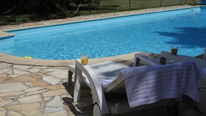 A swimming pool with a stone-tiled deck, a lounge chair with a towel, and a glass of orange juice. - Holiday Home in Quend-Plage near Forest (Quend-Plage)