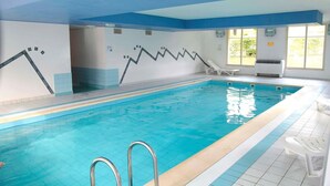 En indendørs swimmingpool med krystalklart vand, et springbræt og et solbelyst rum med et vindue.
