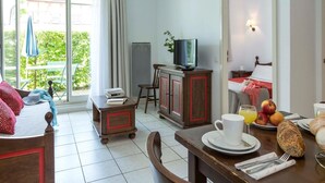 Et hotelværelse med seng, et spisebord med morgenmadsprodukter, et fjernsyn og udsigt til grøn natur.