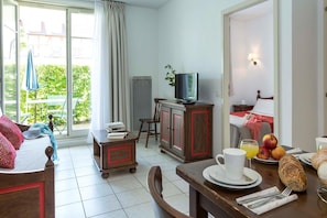 A hotel room with a bed, a dining table with breakfast items, a TV, and a view of greenery outside. - Apartment in Bergheim near Alsace Vineyards (Bergheim)
