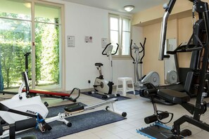 Ein Fitnessstudio mit verschiedenen Trainingsgeräten, darunter ein Rudergerät, ein Crosstrainer und ein Laufband.