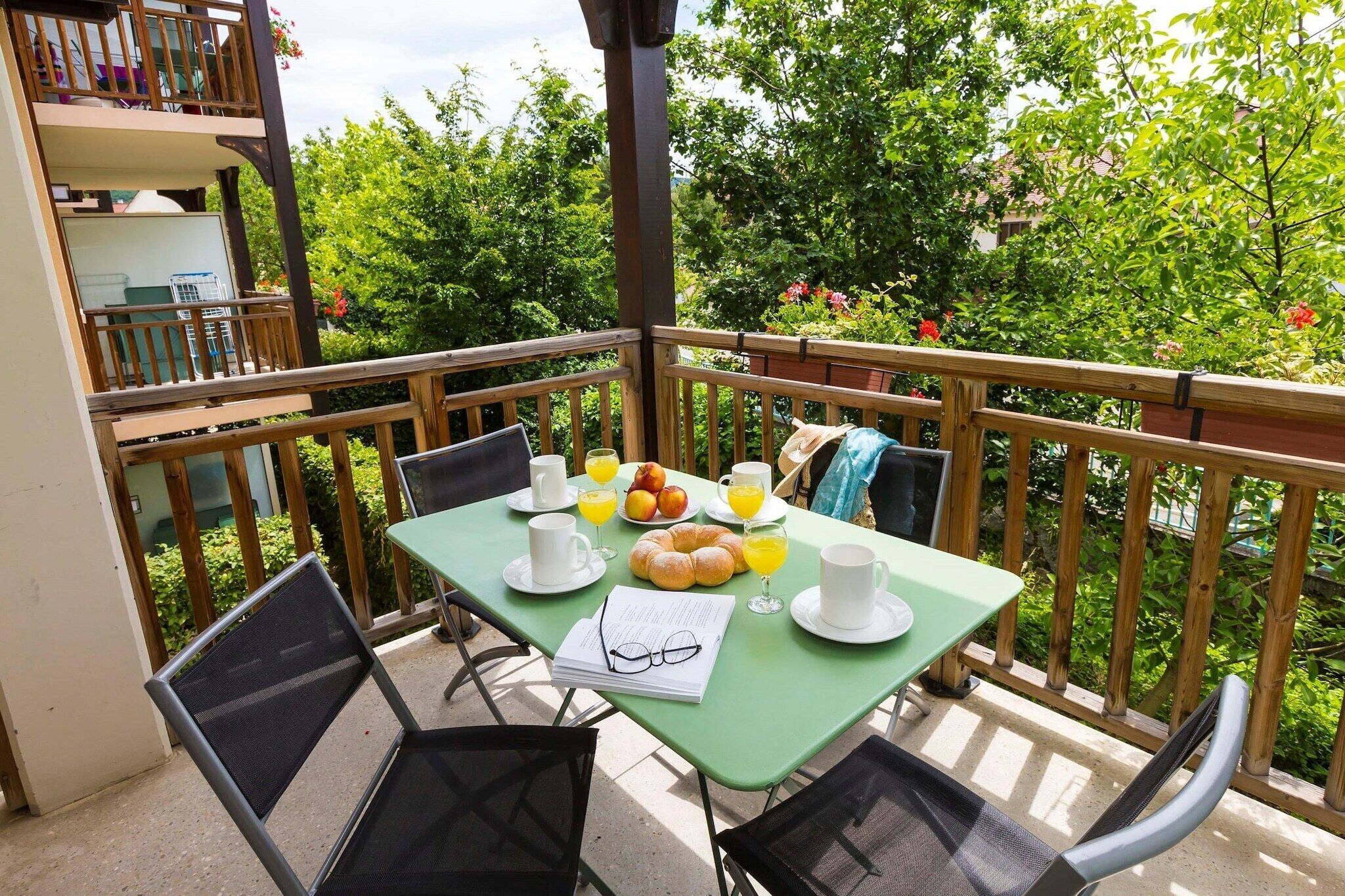 A balcony with a table set for breakfast, including croissants, fruit, and drinks.