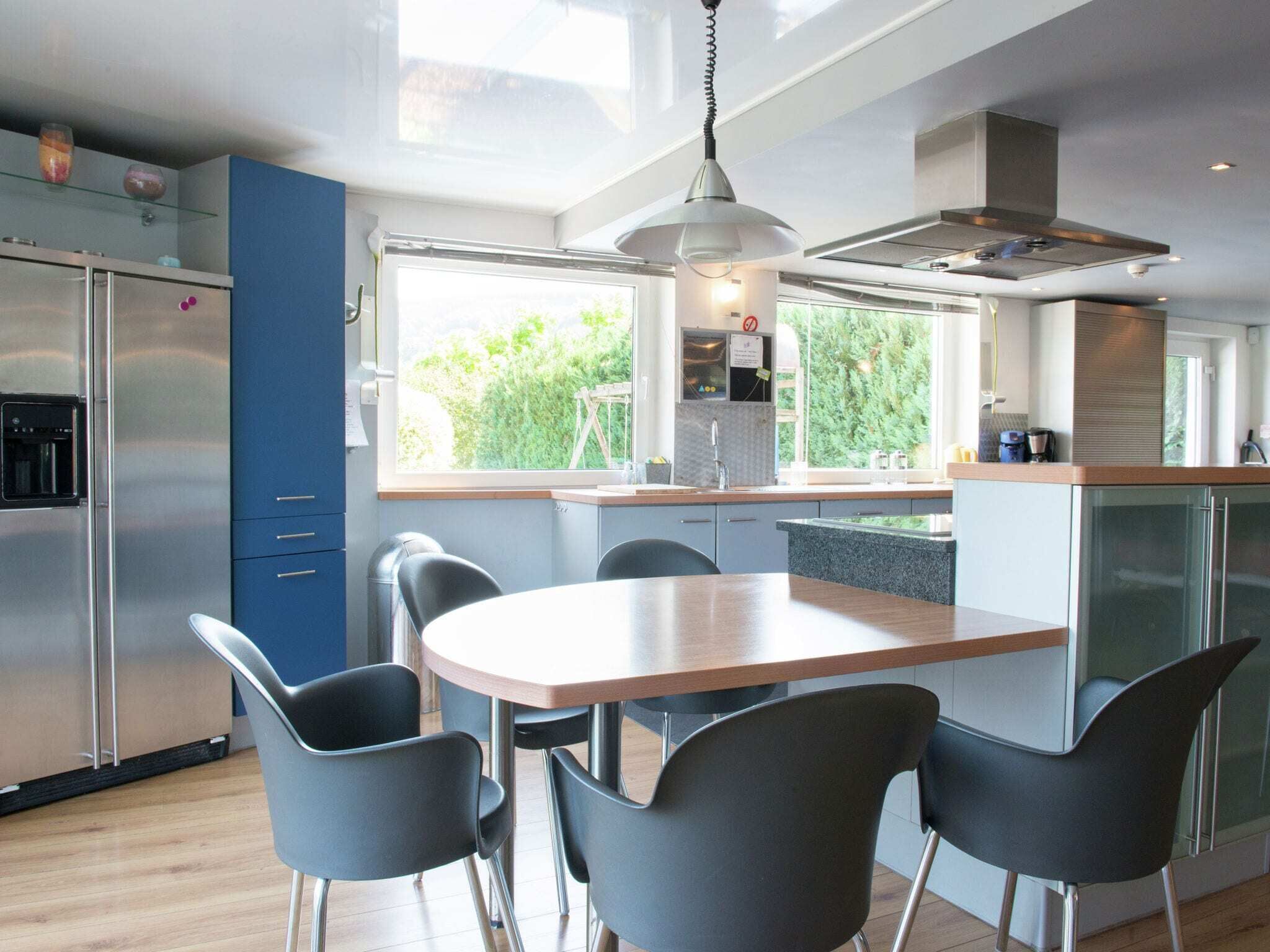 A modern kitchen with a central island, black chairs, and a large window offering a view of greenery.