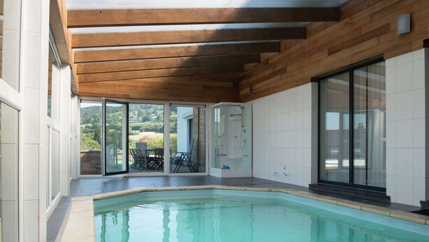 A modern indoor swimming pool with a wooden ceiling and glass doors leading to an outdoor area. - House in Moulin du Ruy with Forest Views (Stoumont-Moulin du ruy)