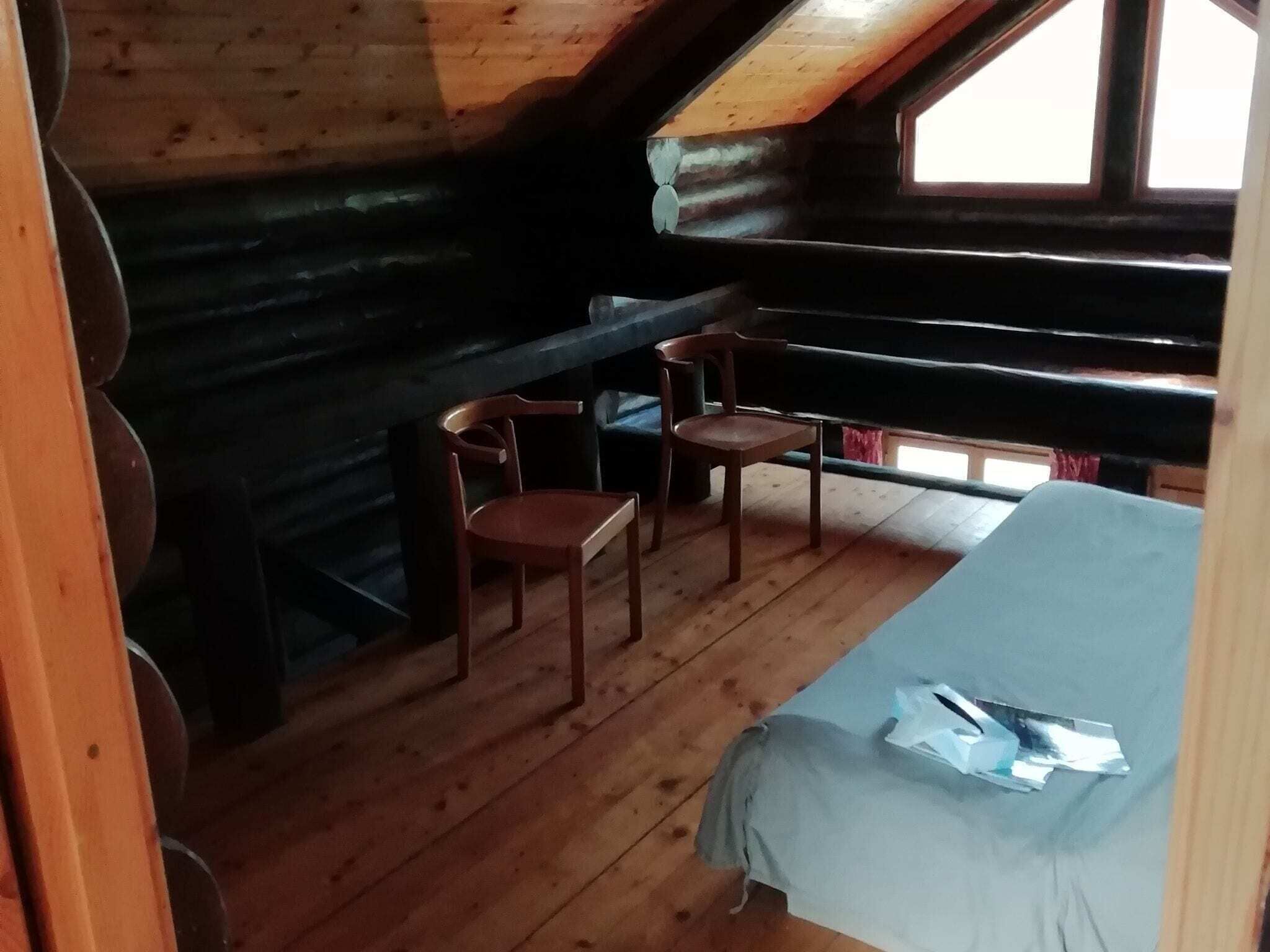 Een chalet met een slaapkamer op de vide, houten wanden, een klein bureau met stoelen en een raam.