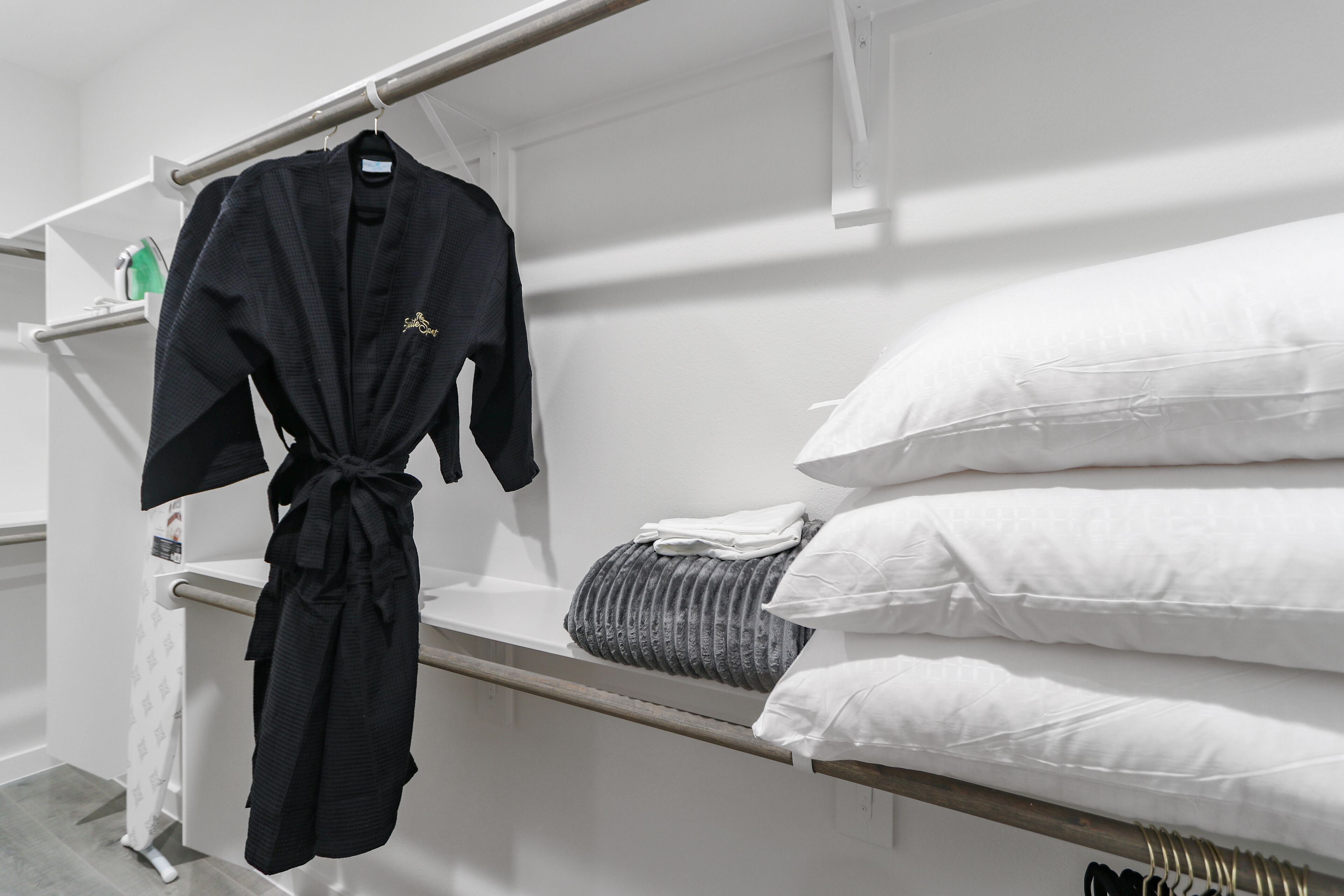 Une chambre d’hôtel avec un lit, des oreillers, un peignoir et une étagère contenant des articles de toilette.