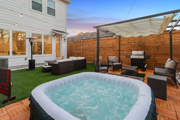 A backyard with a hot tub, outdoor furniture, and a covered patio area.