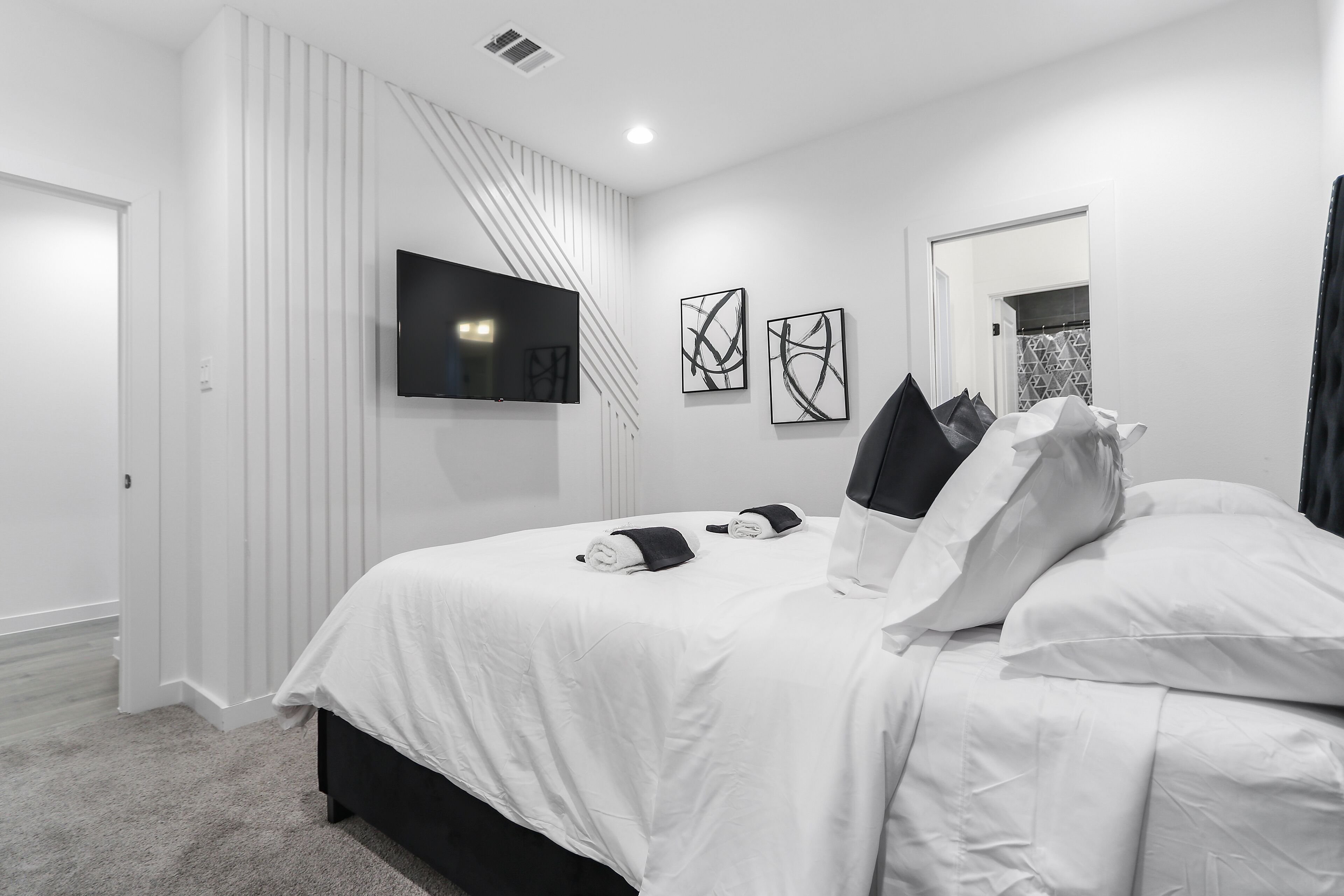 A modern bedroom with a large bed, a flat-screen TV mounted on the wall, and abstract art pieces.