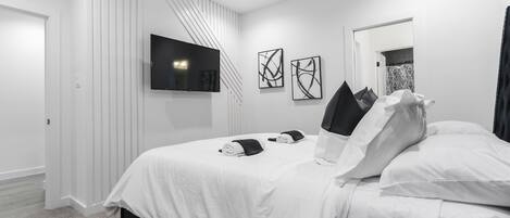 A modern bedroom with a large bed, a flat-screen TV mounted on the wall, and abstract art pieces.