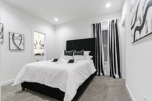Quarto moderno com cabeceira preta, roupa de cama branca e cortinas listradas em preto e branco.