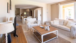 A spacious living area with a wooden coffee table, two white sofas, and a dining area with white chairs. - Holiday Home in Le Plan-de-la-Tour with Pool (Le Plan-De-La-Tour)