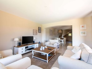 Uma sala de estar moderna com uma televisão de tela plana, uma mesa de centro e um espaço de refeições com cadeiras e uma mesa.
