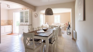 A spacious kitchen with white cabinetry, a dining table with chairs, and a hanging light fixture. - Holiday Home in Le Plan-de-la-Tour with Pool (Le Plan-De-La-Tour)