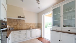 A kitchen with white cabinets, a tiled backsplash, and a glass-fronted cabinet with dishes. - Holiday Home in Le Plan-de-la-Tour with Pool (Le Plan-De-La-Tour)