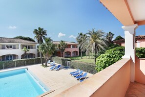 A pool area with lounge chairs, a clear blue pool, and a view of a residential building with a tiled roof.