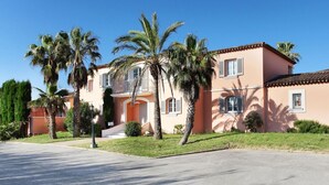 A two-story building with a flat roof, multiple windows with shutters, and a well-maintained lawn with palm trees.
