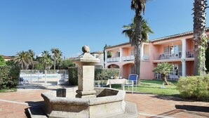 A courtyard with a stone fountain, a pool, and a building with balconies.