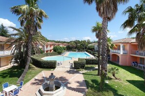 Zona de piscina con cielo despejado, palmeras y un edificio con balcones.