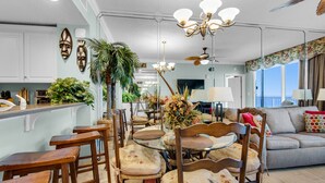 A spacious living area with a dining table surrounded by wooden chairs, a sofa, and a ceiling fan.