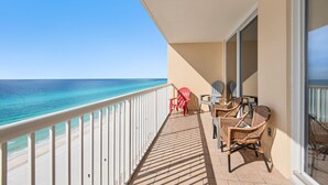 A balcony with a view of the ocean, wicker furniture, and a white railing.