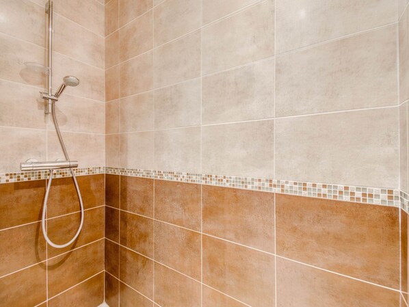 A shower area with a handheld showerhead and a fixed showerhead, tiled walls, and a mosaic border.