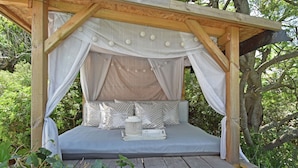 Ein hölzernes Baldachinbett mit grauem Matratze, weißer Bettwäsche und einem kleinen Tisch mit Büchern.