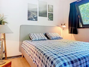 Ein Schlafzimmer mit einem Bett, einer Lampe, einem Blumentopf und einem Fenster mit Vorhängen.