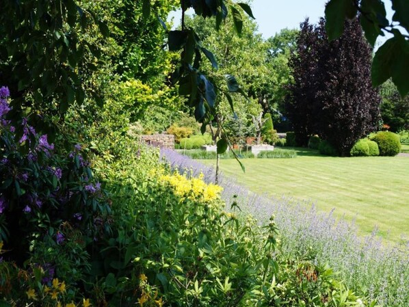 A well-maintained garden with a variety of flowering plants, neatly trimmed grass, and a stone wall in the background. - Chalet in Belgium surrounded by nature (Oignies en Thiérache)