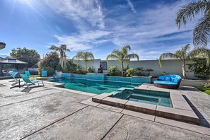 Ein Pool mit einer Sitzecke im Wasser, umgeben von Palmen und einer Liege.