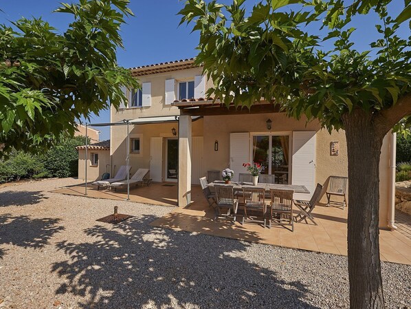 Una casa de dos pisos con un patio, mobiliario exterior y una pérgola.